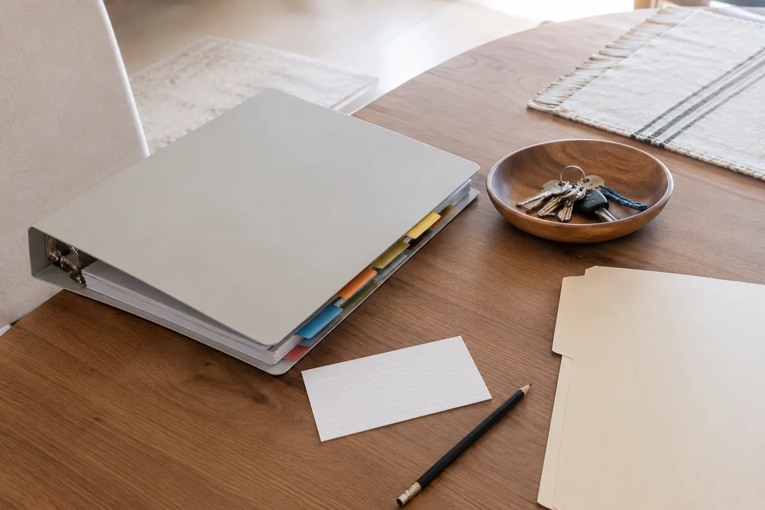 A neutral binder with colored dividers, a blank note card, folder, pencil, and keys on a home table.