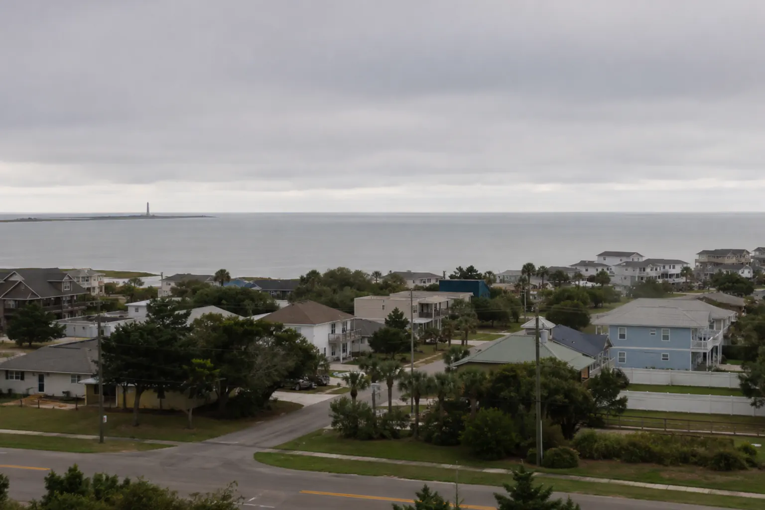 A low-lying coastal neighborhood seen from an elevated vantage under an overcast pre-storm sky, the water calm and no flooding present.