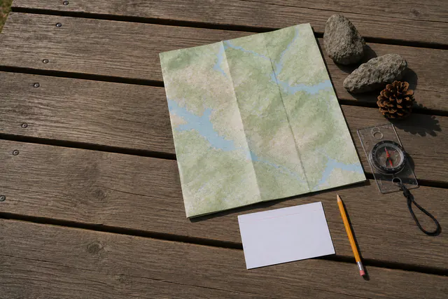 An overhead view of an unfolded practice map showing only abstract contour-like colour fields with no labels, beside a plain baseplate compass, on an outdoor picnic table.