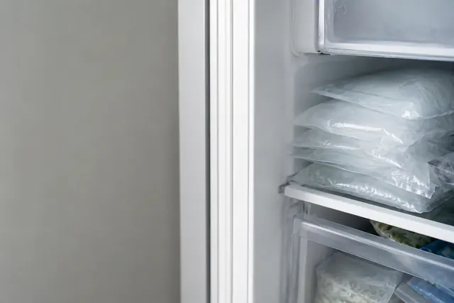 Sealed bags of ice stacked on a freezer shelf above frozen food.