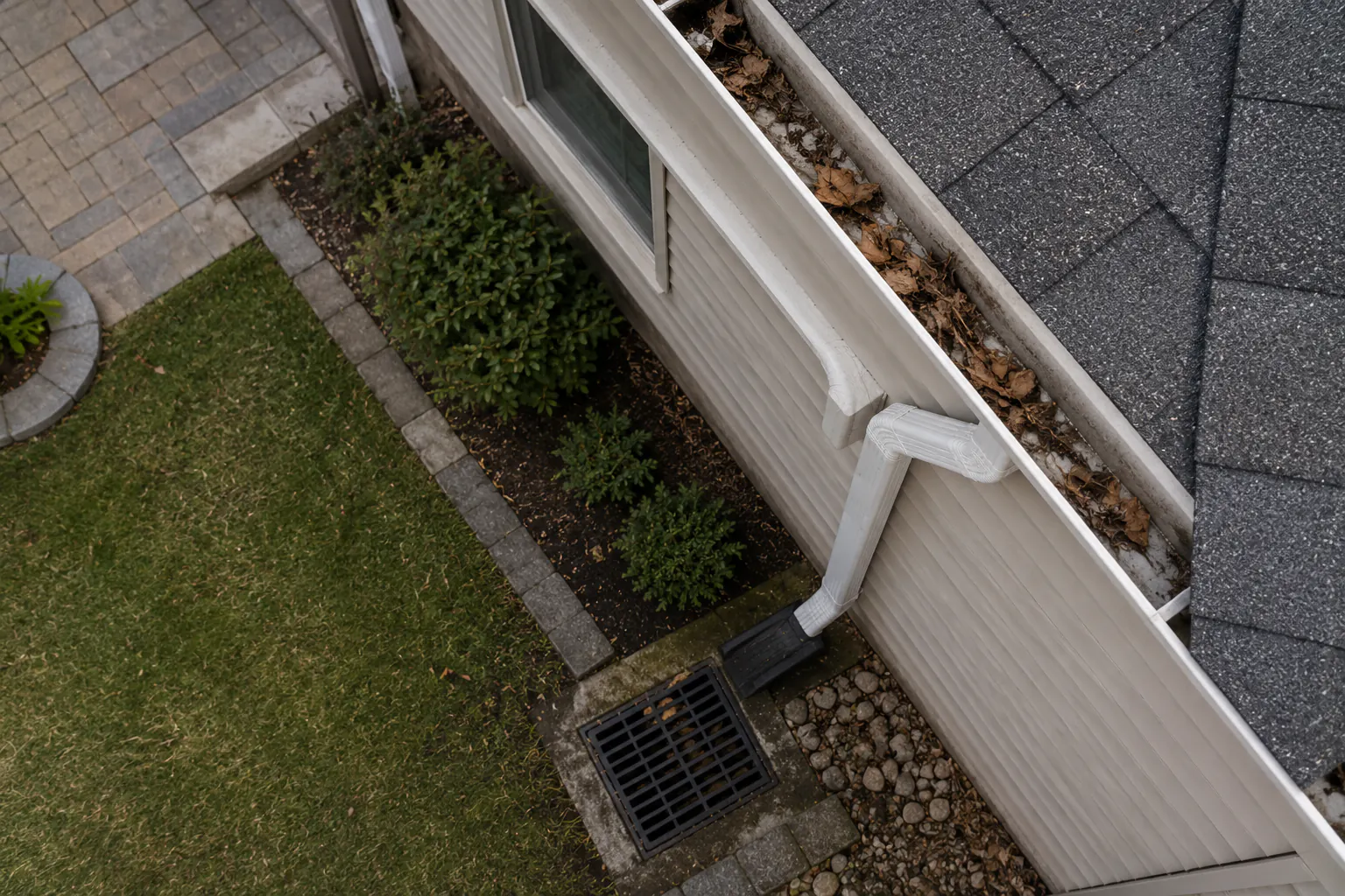 Downspout directing water into a drain beside a house.