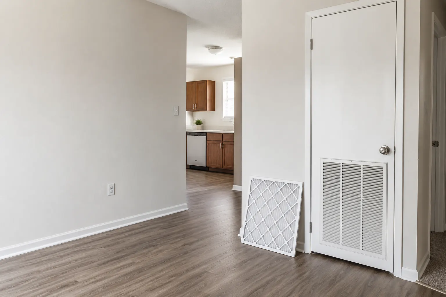 A closed HVAC closet door with a return-air grille and a new air filter leaning against the wall beside it.