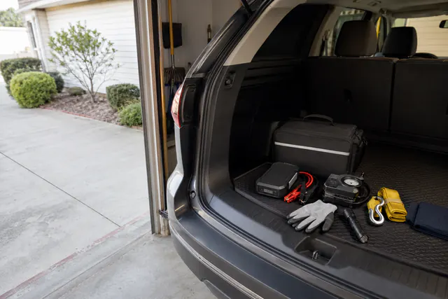 Jump starter, gloves, straps, and compact emergency gear arranged in an SUV cargo area.